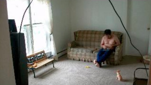 Picture of the living room. A guy in jeans and no shirt is on the couch. Also a chihuahua.